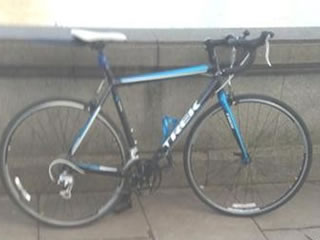 bicycle is blue with curved handle bars, a white saddle and the word 'Trek' written in white